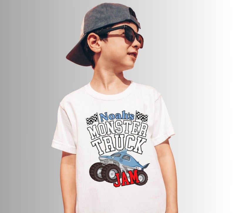 Puede incluir: Camiseta blanca con un gr&aacute;fico de monster truck. El dise&ntilde;o presenta un cami&oacute;n con tem&aacute;tica de tibur&oacute;n con el texto "Noah's MONSTER TRUCK JAM". La camiseta tiene cuello redondo y mangas cortas.