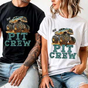 May include: Black and white t-shirt featuring a monster truck graphic with a checkered flag and the words "PIT CREW" in teal. The monster truck is beige, blue, and brown.