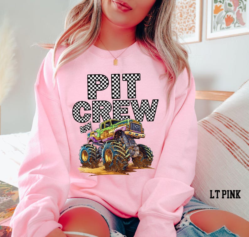 Pictured is a woman wearing a pink sweatshirt with black and white checkered graphic letters that say "PIT CREW" and a cartoon purple and green monster truck.