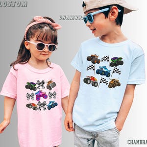 May include: Two children wearing light-colored t-shirts with monster truck graphics. The pink shirt features a variety of trucks and checkered bows. The blue shirt displays monster trucks with checkered flags. The word "BLOSSOM" is printed at the top left, and "CHAMBRAY" is printed at the bottom right.