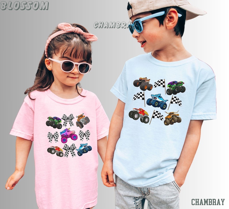May include: Two children wearing light-colored t-shirts with monster truck graphics. The pink shirt features a variety of trucks and checkered bows. The blue shirt displays monster trucks with checkered flags. The word "BLOSSOM" is printed at the top left, and "CHAMBRAY" is printed at the bottom right.