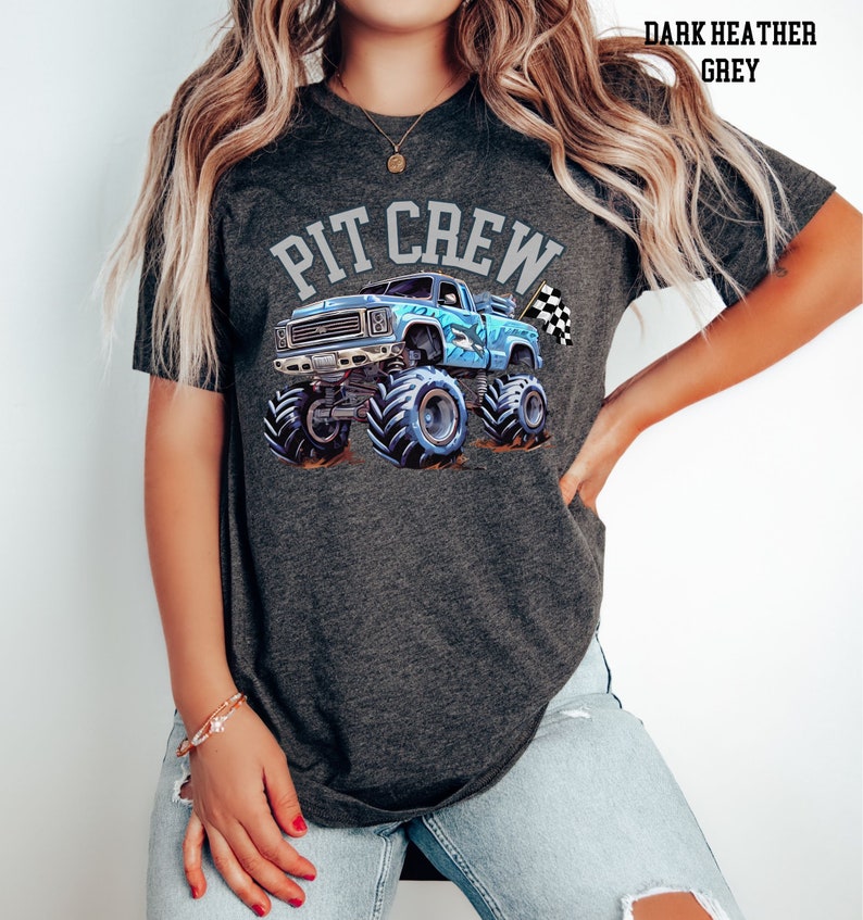 Pictured is a woman wearing a dark gray charcoal t-shirt which says "PIT CREW" in college varsity letters in light gray color. There is a blue monster truck with a shark on the side with a checkered flag. Suitable for parent of a birthday party child.