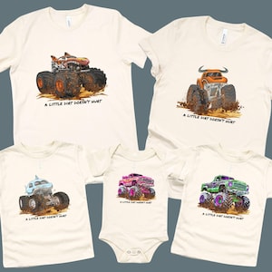 Puede incluir: Camisetas y un body color crema con diseños de monster trucks coloridos. Cada prenda muestra un camión diferente, incluyendo un tiburón, un toro y un camión con un diseño de llama. El texto "A LITTLE DIRT DOESN'T HURT" está impreso debajo.