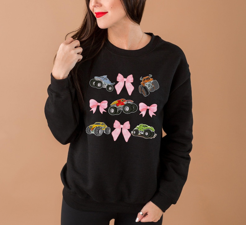 woman model is wearing a black monster truck jam Girls Woman's Sweatshirt with 5 monster trucks and 4 Pink Coquette Bows Long-Sleeve Sweaters: Family Matching Long-sleeved monster truck shirts outfits. Adult, teen, youth, toddler and infant sizes.