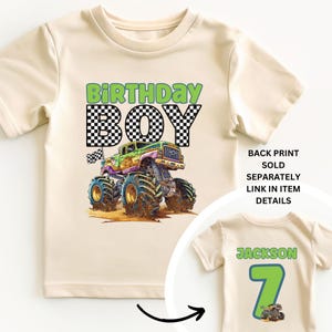 May include: Cream-colored t-shirt featuring a colorful monster truck graphic with the text "BIRTHDAY BOY". The design includes a checkered pattern and a small checkered flag. A second shirt shows a back print with the name "Jackson" and the number "7".