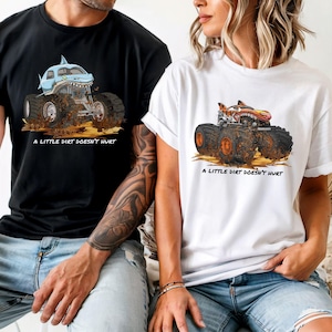 May include: Black and white t-shirts with monster truck graphics. One shirt features a blue shark-themed truck, the other an orange and red truck. Both shirts have the text "A LITTLE DIRT DOESN'T HURT" below the graphic.