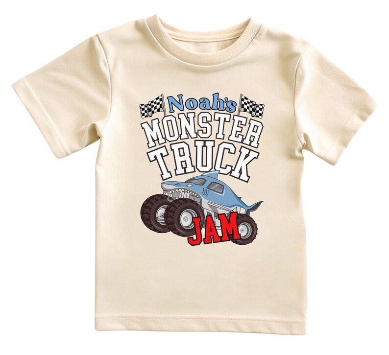 以下が含まれることがあります： クリーム色のTシャツ。大胆なフォントで「Noah's MONSTER TRUCK JAM」と書かれています。デザインには、大きな車輪とチェッカーフラッグを備えたサメ型のモンスタートラックが含まれています。「JAM」という単語は赤色です。