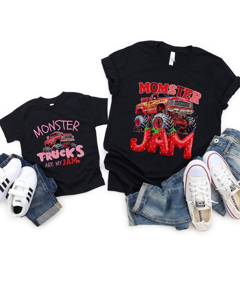 Two black T-shirts one child sized says "MONSTER TRUCKS ARE MY JAM" in pink and strawberry letters with a red monster truck. The adult sized one says "MOMSTER JAM" in strawberry letters with a red monster rtuck