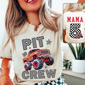 Op de afbeelding: Beige T-shirt met een rode monstertruck-afbeelding, vlammen en de woorden "PIT CREW" in een dambordpatroon. De achterkant van het shirt heeft het woord "MAMA" en het nummer "5" met een monstertruck-afbeelding.