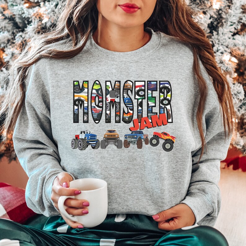 May include: Gray sweatshirt with the text "MOMSTER JAM" in colorful letters. The letters are made up of images of monster trucks.
