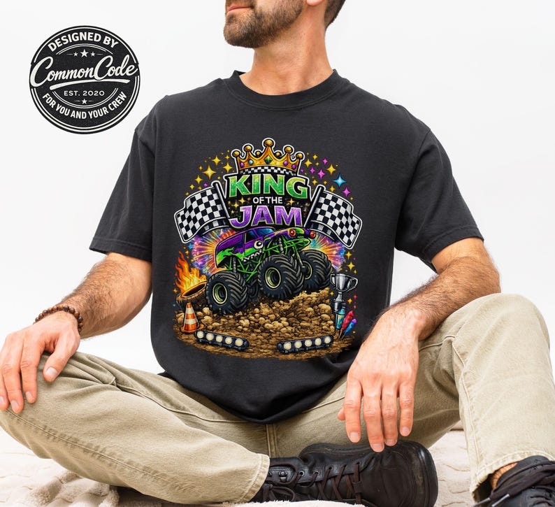 Peut inclure: T-shirt noir avec un motif color&eacute; d'un monster truck et le texte "KING OF THE JAM". Le design comprend des drapeaux &agrave; damier, une couronne et le logo Common Code.
