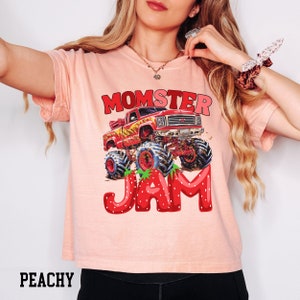 May include: A pink t-shirt with a graphic of a red monster truck with flames and the text "MOMSTER JAM" in red letters with strawberry accents.