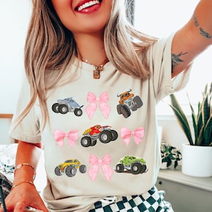 natural cream colored t-shirt with pink bows and monster trucks collage grid style 3x3. Shark Truck, Bull toro truck, dinosaur truck, mutt truck, red dragon truck. Perfect for Monster truck Jam and Car and Truck shows and races. Perfect gift for mommy and mini matching bow shirts with a fun girl power flare.