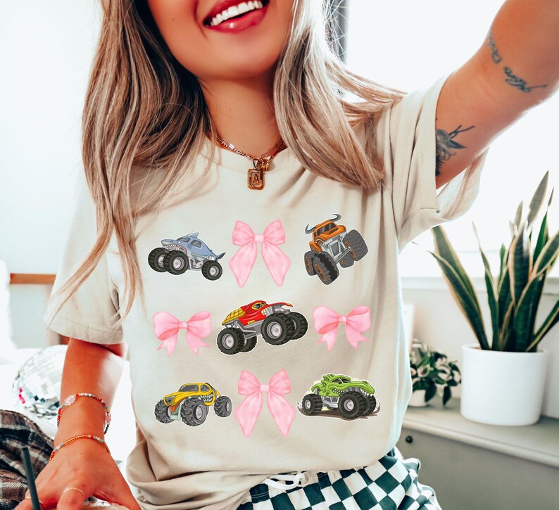 natural cream colored t-shirt with pink bows and monster trucks collage grid style 3x3. Shark Truck, Bull toro truck, dinosaur truck, mutt truck, red dragon truck. Perfect for Monster truck Jam and Car and Truck shows and races. Perfect gift for mommy and mini matching bow shirts with a fun girl power flare.