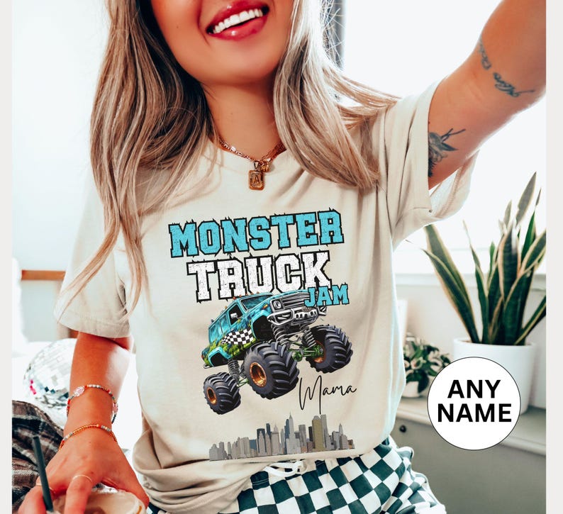 Model is wearing a natural colored t-shirt that says This" Monster Truck Jam" in Blue Letters With Black and White Checkered Flag On The Side With Big Tires Wheels Is Doing Stunts and Jumping Over The City Skyline Getting Big Air At The Jam This Shirt is Custom Personalized With Name Signature.  get one For each member Of the Family and Wear To the Big Event