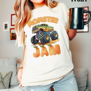 May include: A white t-shirt with a green monster truck graphic and the text "Momster Jam" in orange letters. The truck is driving over orange peaches.