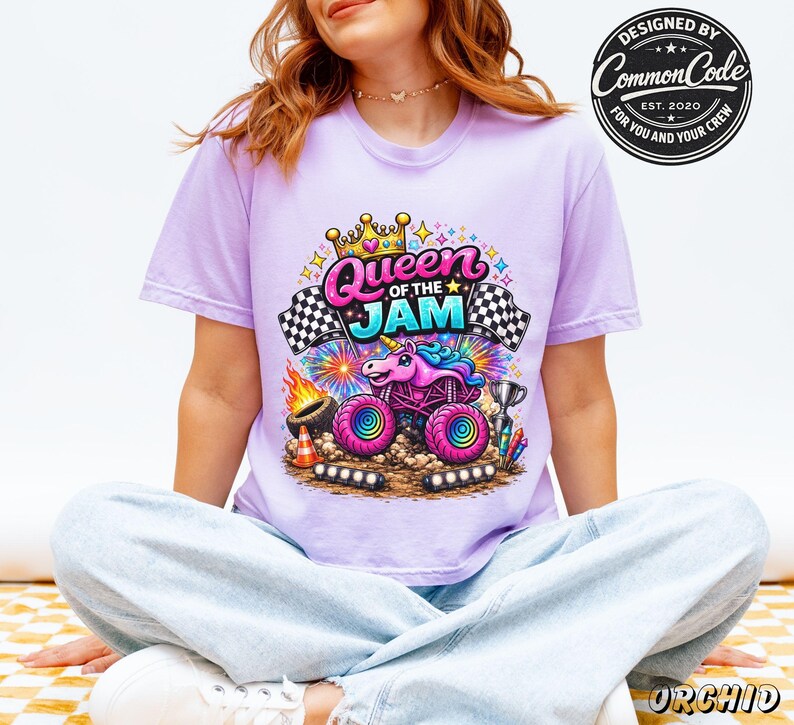 Peut inclure: Un t-shirt lilas avec un graphisme color&eacute; d'un monster truck avec un design de licorne et le texte "Queen of the Jam". Le design comprend des drapeaux &agrave; damier, des feux d'artifice et les mots "Designed by Common Code".
