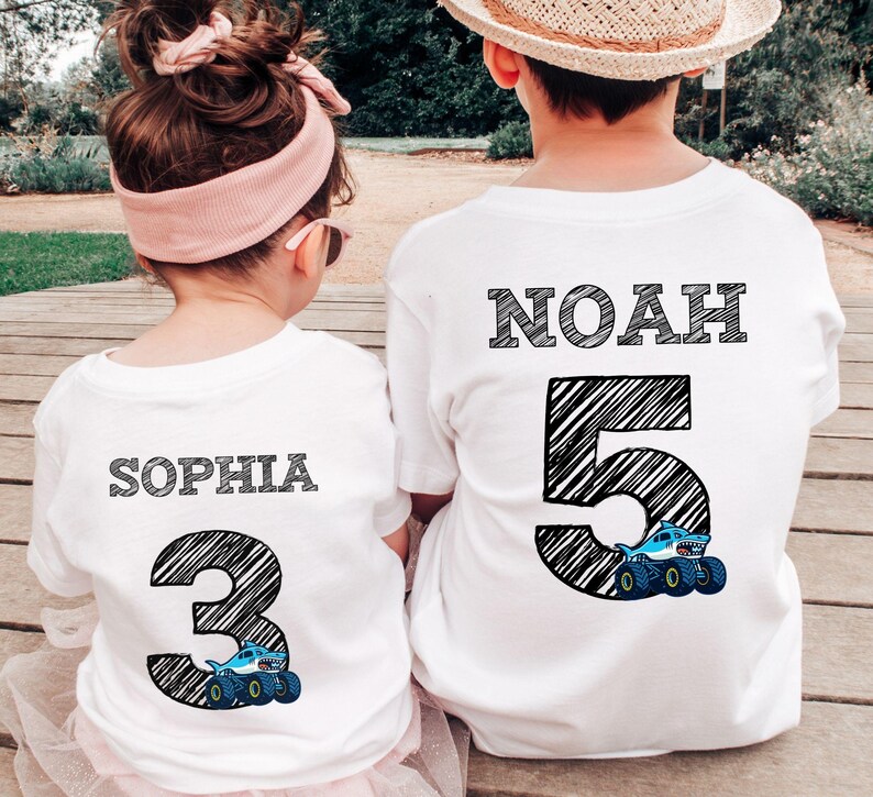 Op de afbeelding: Twee witte T-shirts. E&eacute;n shirt heeft de naam "SOPHIA" boven een groot nummer "3" met een monster truck-afbeelding. De andere heeft "NOAH" boven een groot nummer "5" met een monster truck-afbeelding. De tekst en nummers zijn zwart.