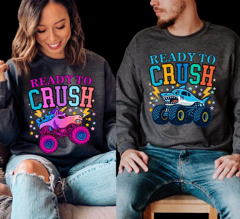 Pu&ograve; includere: Due felpe grigio scuro con la scritta "READY TO CRUSH". Una felpa presenta un monster truck unicorno, l'altra un monster truck squalo. Entrambi i design hanno accenti colorati e stelle.
