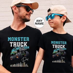 May include: Two black t-shirts featuring a monster truck graphic and the text "Monster Truck Jam". The larger shirt says "Dad" and the smaller shirt says "Noah".