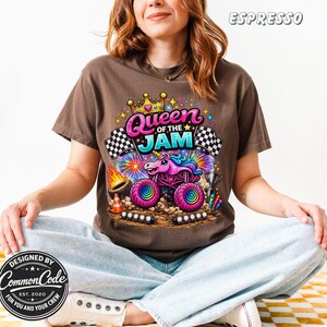Peut inclure: T-shirt couleur expresso avec un motif color&eacute; d'un monster truck avec un design de licorne, le texte "Queen of the Jam" et des drapeaux &agrave; damier. Le t-shirt est con&ccedil;u par Common Code.