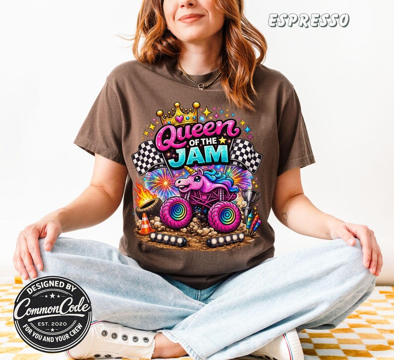 Peut inclure: T-shirt couleur expresso avec un motif color&eacute; d'un monster truck avec un design de licorne, le texte "Queen of the Jam" et des drapeaux &agrave; damier. Le t-shirt est con&ccedil;u par Common Code.