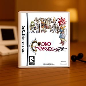 May include: A white Nintendo DS game case featuring the game "Chrono Trigger." The cover art displays several animated characters in a fantasy setting. The game's title is prominently displayed in a stylized font. The case has a "12+" rating.