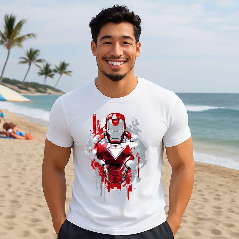 Puede incluir: Camiseta blanca con un gr&aacute;fico de la armadura de Iron Man en rojo, plateado y blanco. El dise&ntilde;o es una ilustraci&oacute;n estilizada con un efecto de salpicadura. La camiseta la lleva una persona en una playa.