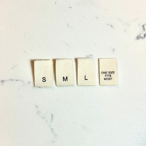 May include: Four white fabric tags with black text. The tags read "S", "M", "L", and "One Size Fits Most".