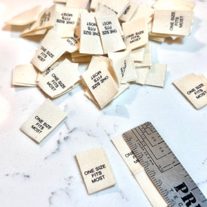 May include: A pile of white fabric tags with black text that reads "One Size Fits Most".