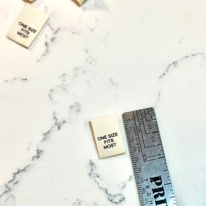 May include: A white fabric label with black text that reads "ONE SIZE FITS MOST". The label is measured with a ruler.