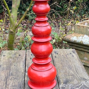 May include: A vibrant red candlestick with a tiered, rounded design. The decorative piece is made of a glossy material and sits on a wooden surface. The candlestick is approximately 46 cm tall.