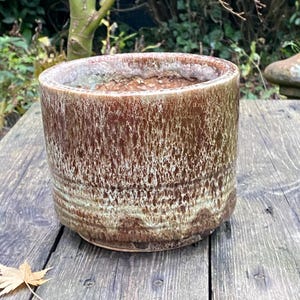 May include: A brown and white ceramic planter with a textured glaze. The planter has a wide, round opening and a slightly flared lip.