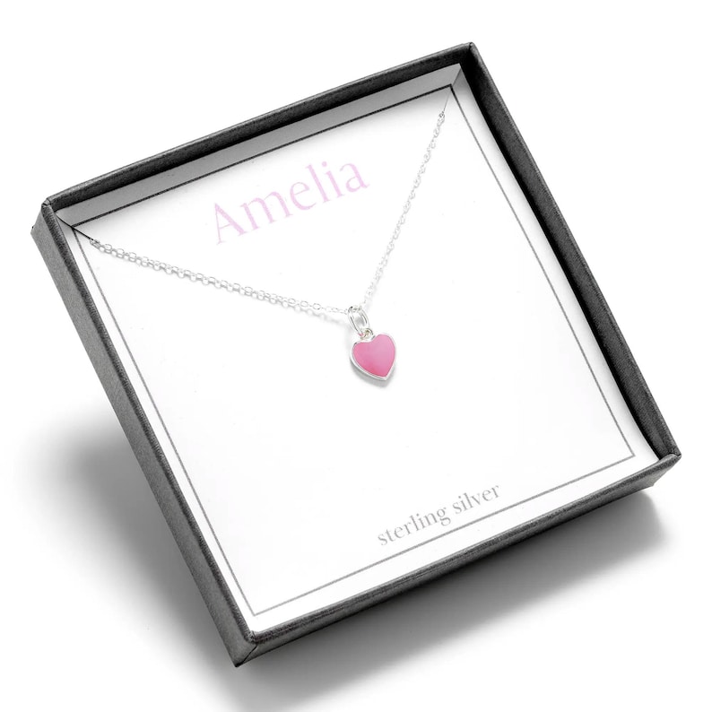May include: A silver necklace with a pink heart pendant in a gift box. The box has the name "Amelia" and the words "sterling silver" printed on it.