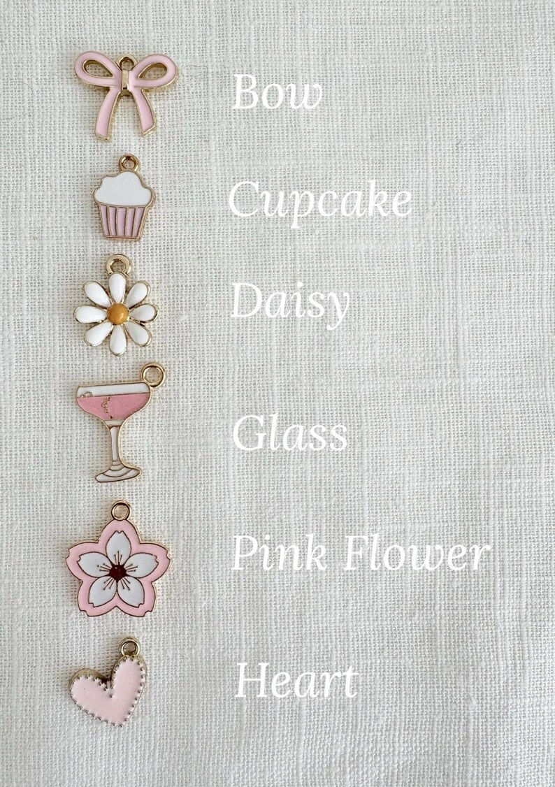 May include: A collection of pink and gold charms, including a bow, cupcake, daisy, glass, pink flower, and heart. Each charm is detailed with enamel and has a loop for attaching to jewelry or other crafts. Text labels each charm.