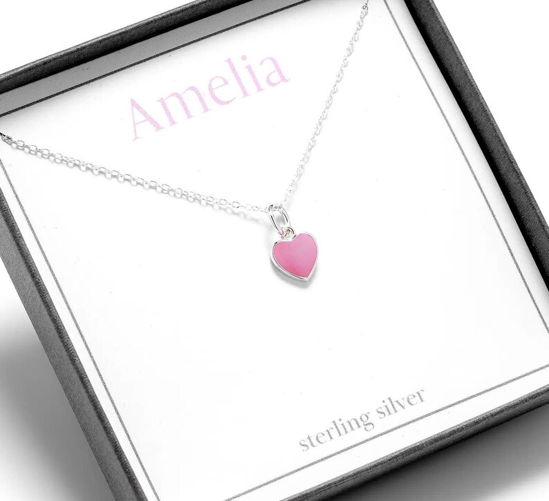 May include: A silver necklace with a pink heart pendant. The necklace is in a box with the name Amelia and the words "sterling silver" written on it.