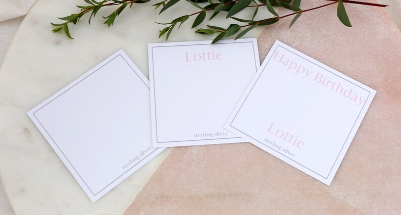 May include: Three white gift tags with black borders. The top tag says "Happy Birthday" in pink lettering. The middle tag says "Lottie" in pink lettering and "sterling silver" in black lettering. The bottom tag says "Lottie" in pink lettering and "sterling silver" in black lettering.