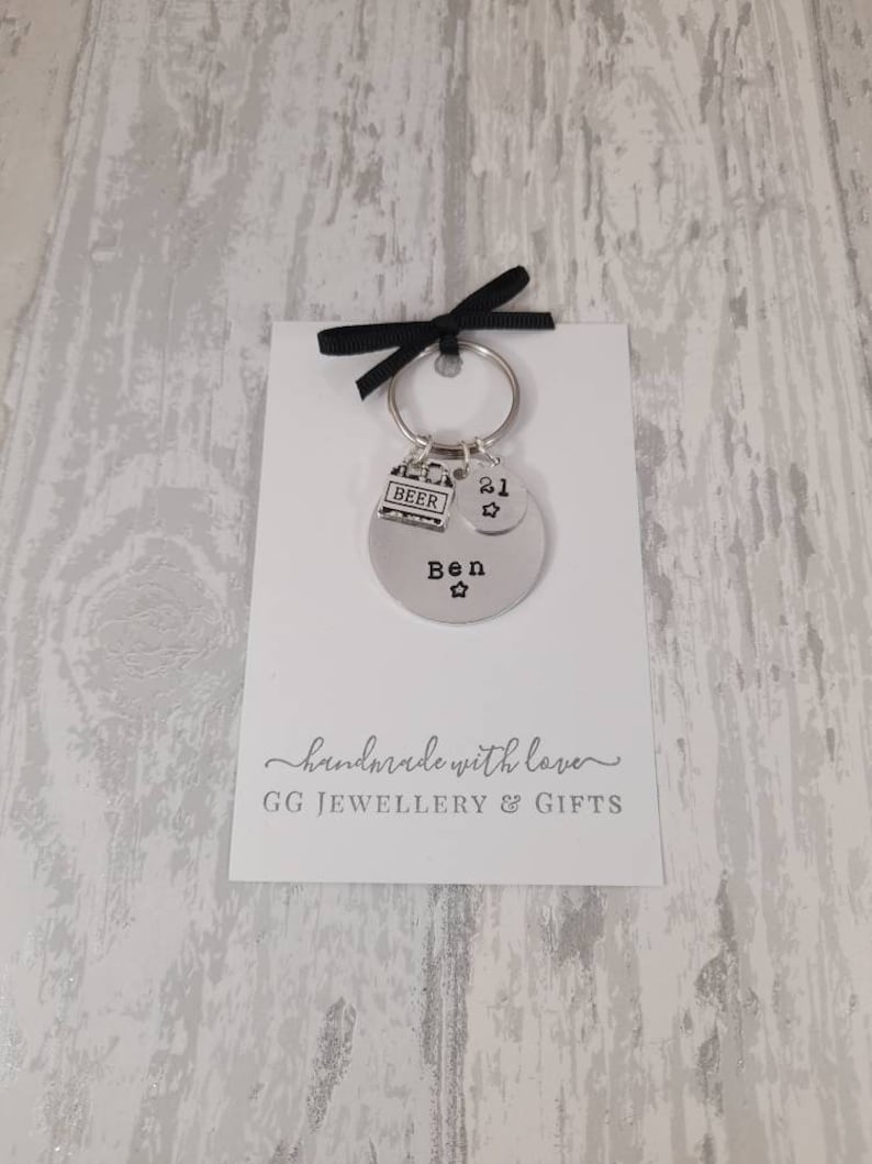 May include: A silver keychain with a round charm that says "Ben" with a star, a charm that says "21" with a star, and a charm that says "Beer". The keychain is on a white card with the text "handmade with love GG JEWELLERY & GIFTS".