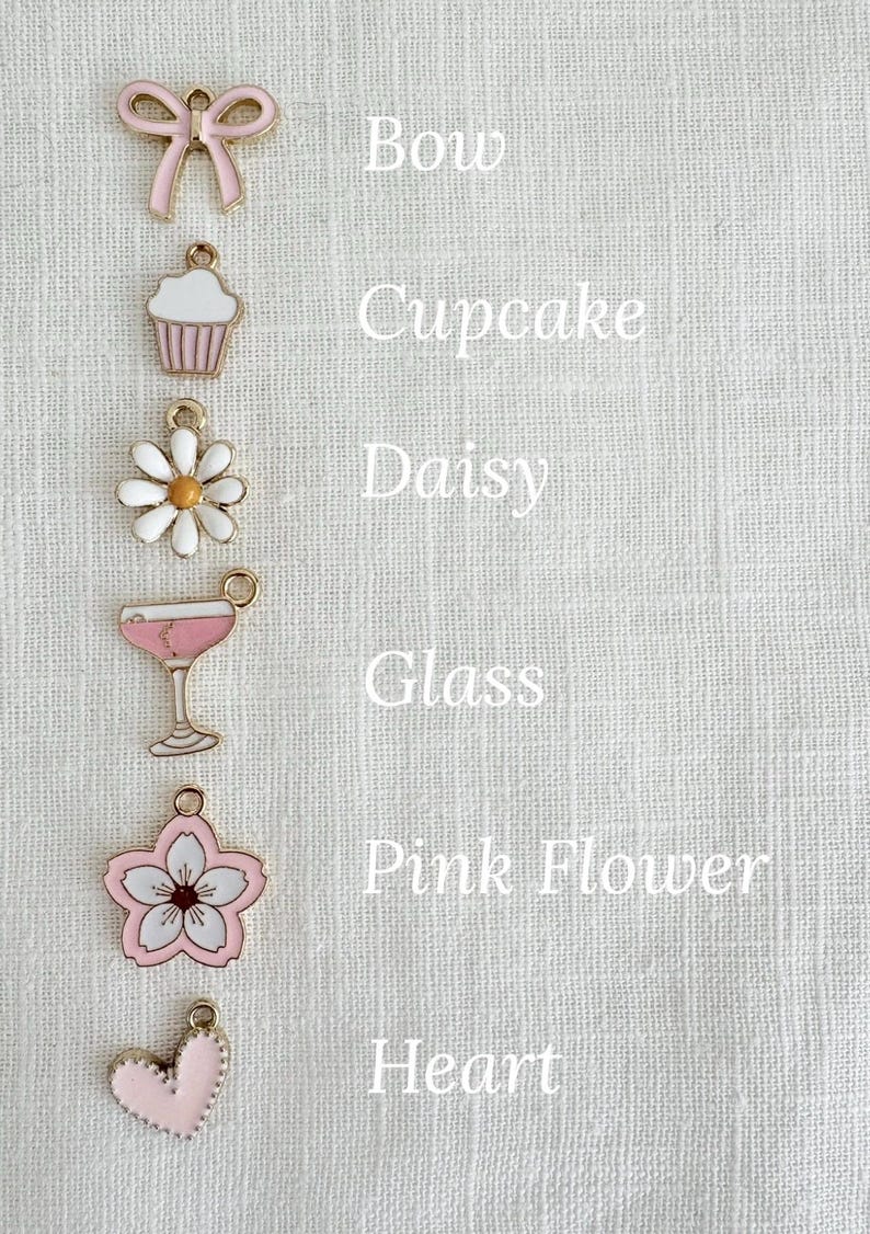 Pu&ograve; includere: Sei ciondoli diversi in metallo dorato e smalto. I ciondoli hanno la forma di un fiocco, un cupcake, una margherita, un bicchiere, un fiore rosa e un cuore. Tutti i ciondoli sono rosa e bianchi.