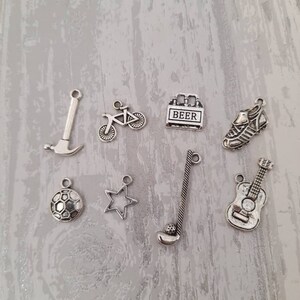 May include: A set of eight silver charm pendants featuring various designs, including a bicycle, a soccer ball, a guitar, a star, a hammer, a golf club, a beer bottle, and a soccer cleat.