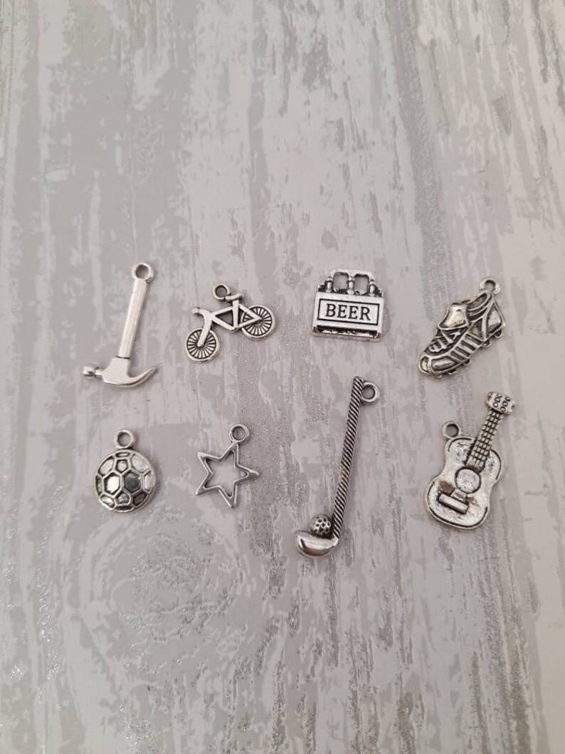 May include: A set of eight silver charm pendants featuring various designs, including a bicycle, a soccer ball, a guitar, a star, a hammer, a golf club, a beer bottle, and a soccer cleat.