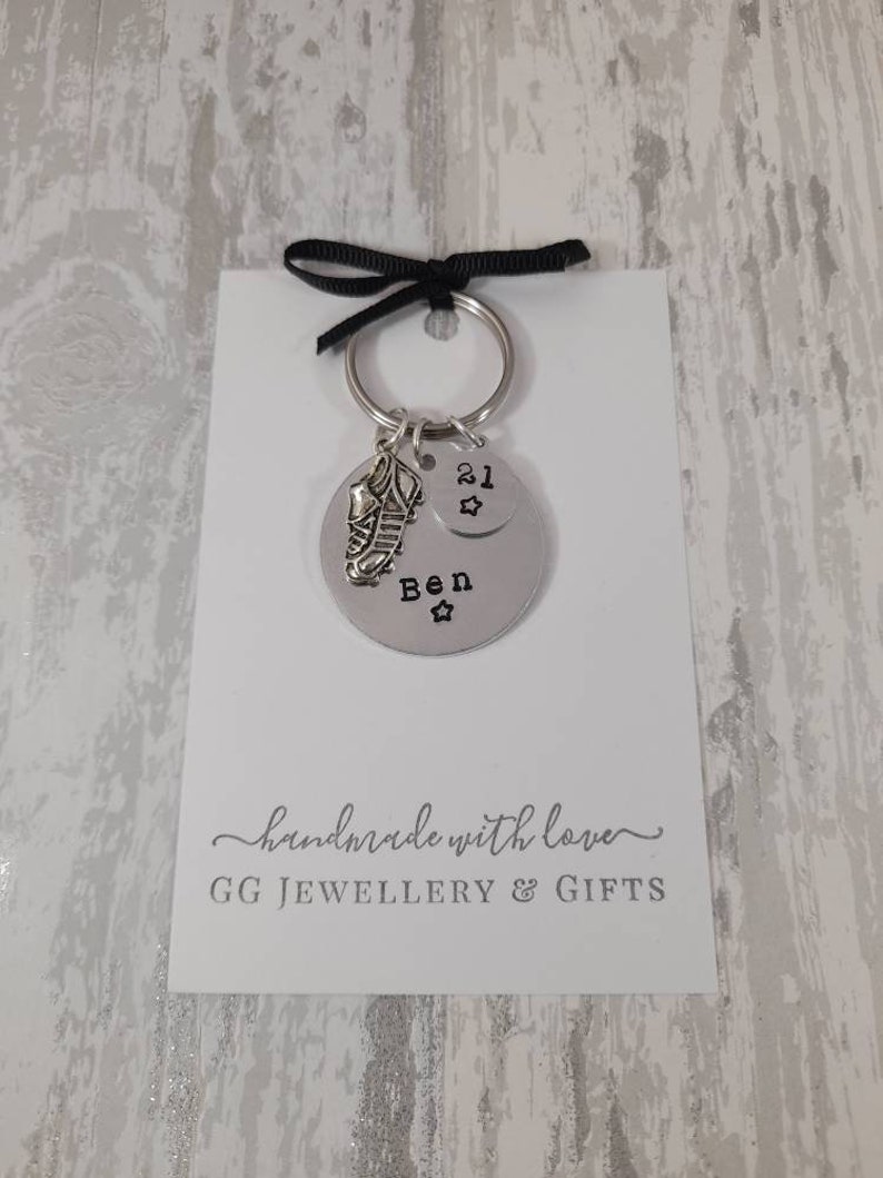 May include: Silver keychain with a football boot charm and a round tag that says "Ben 21" with a star. The keychain is on a white card with the text "handmade with love GG JEWELLERY & GIFTS".