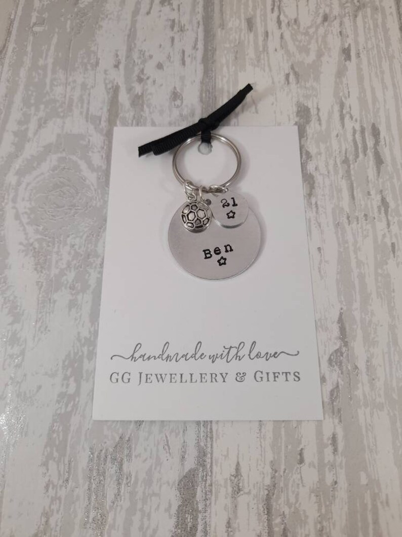 May include: Silver keychain with a soccer ball charm, a charm with the number 21, and a charm with the name "Ben" on it. The keychain is on a white card with the text "handmade with love GG JEWELLERY & GIFTS".
