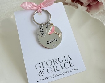 Op de afbeelding: Een zilveren sleutelhanger met een roze cocktailbedel, een hartbedel met het nummer 21 en een rond label met de tekst "Chloe" met een hart. De sleutelhanger bevindt zich op een witte kaart met de tekst "GEORGIA & GRACE" en "www.georgiaandgrace.co.uk".