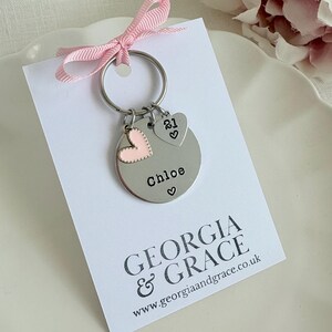 Pu&ograve; includere: Un portachiavi d'argento con un ciondolo a forma di cuore e un ciondolo rotondo che dice "Chloe" con un cuore. Il portachiavi &egrave; su una carta bianca con il testo "GEORGIA & GRACE www.georgiaandgrace.co.uk"