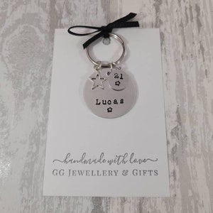 May include: Silver keychain with a star charm and a round tag that says "Lucas" and "21" with a star. The keychain is on a white card with the text "handmade with love" and "GG JEWELLERY & GIFTS".