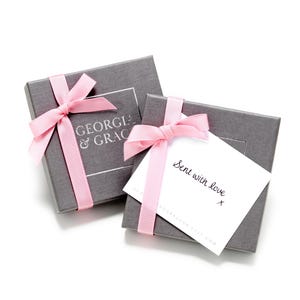 May include: Two gray gift boxes with pink ribbon bows. The top box has a white label with the text "GEORGIA & GRACE". The bottom box has a white card with the text "Sent with love" and a handwritten signature.