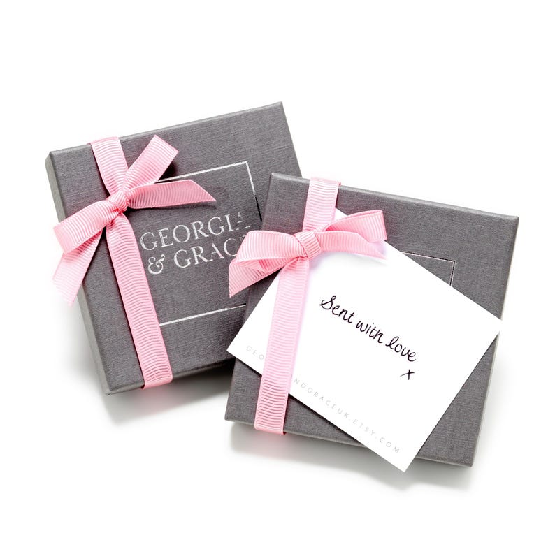 May include: Two gray gift boxes with pink ribbon bows. The top box has a white label with the text "GEORGIA & GRACE". The bottom box has a white card with the text "Sent with love" and a handwritten signature.