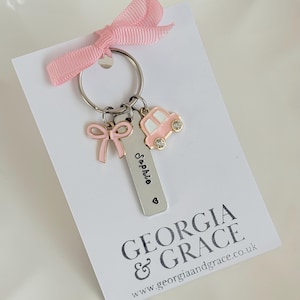 May include: A pink and silver keychain with a car charm, a bow charm, and a personalized tag that says "Sophie". The keychain is on a white card with the text "GEORGIA & GRACE www.georgiaandgrace.co.uk"