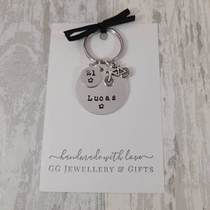 May include: Silver keychain with a round charm that says "Lucas" and a smaller charm with the number "21" and a star. The keychain also has a small charm of a bicycle. The card attached to the keychain says "handmade with love GG JEWELLERY & GIFTS".